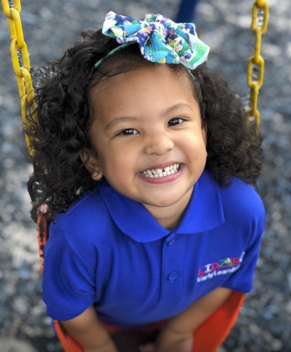 A smiling girl looking up from the swings at the Early Learning Center